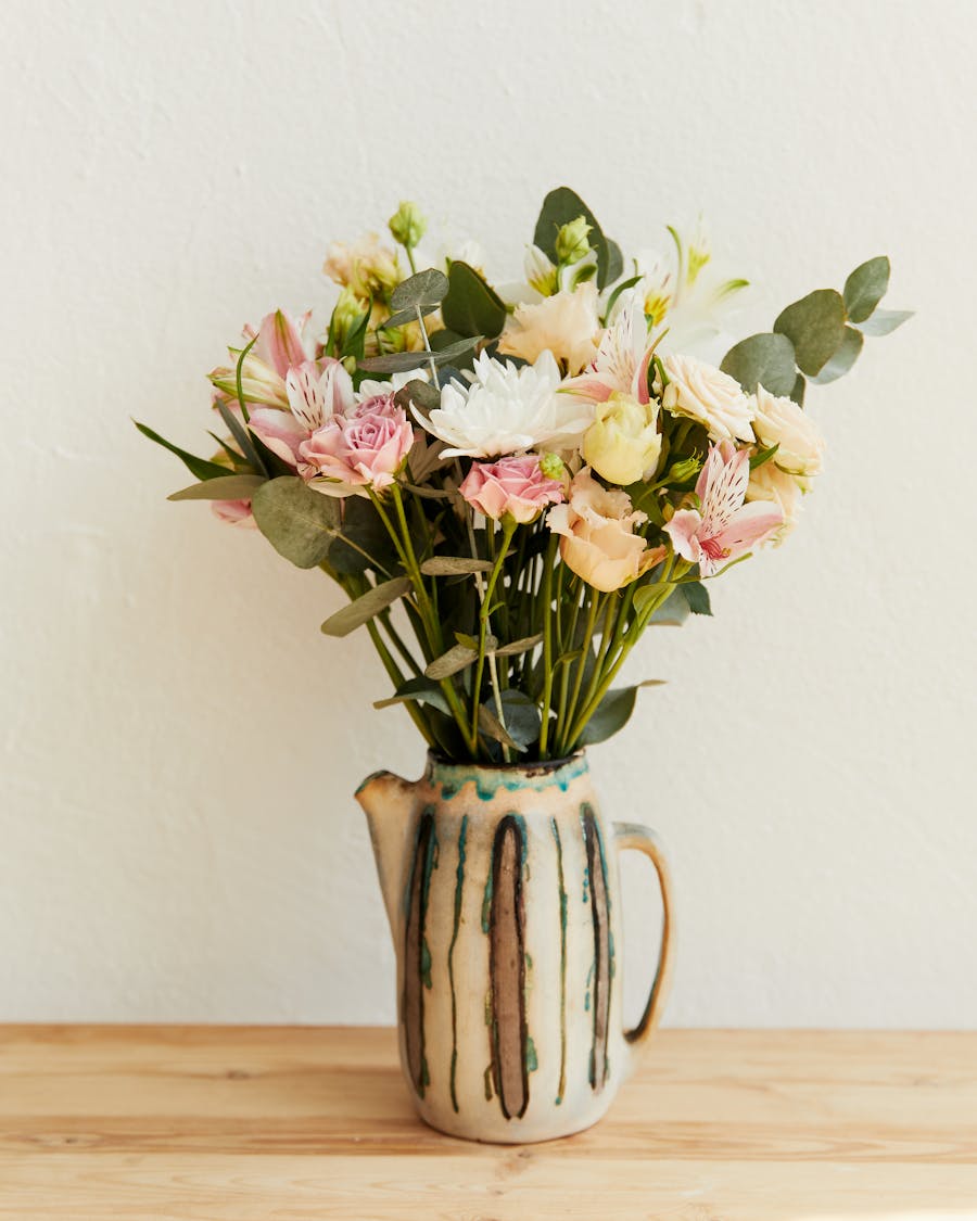 A flower bouquet arranged in a ceramic jug on a wooden table